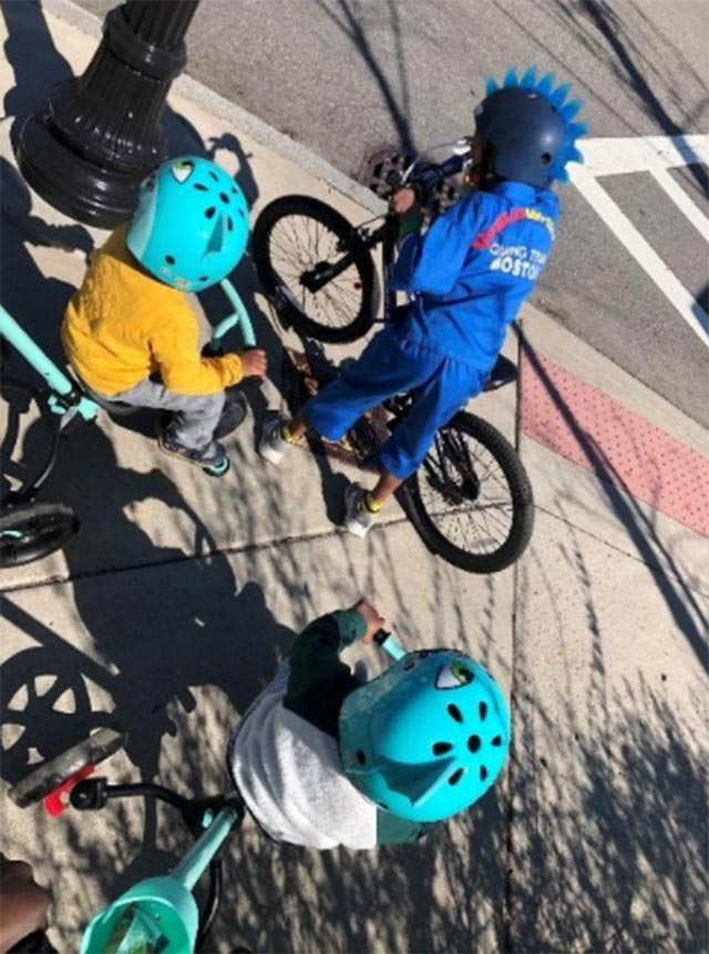 Kids wearing colorful helmets on their bikes at a street corner.