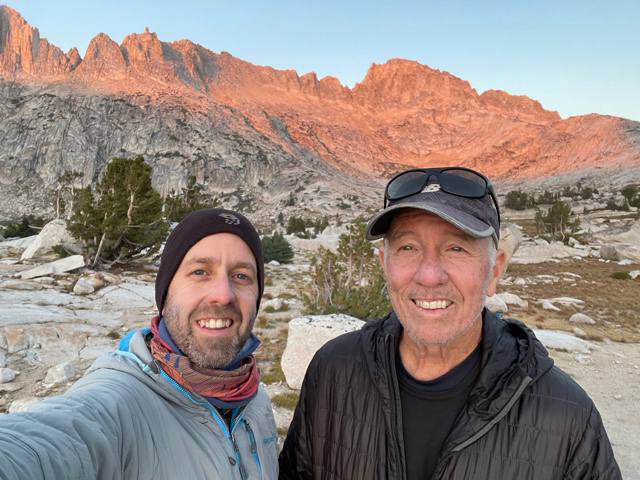 Two men smiling at the camera in front of a beautiful red rock landscape.