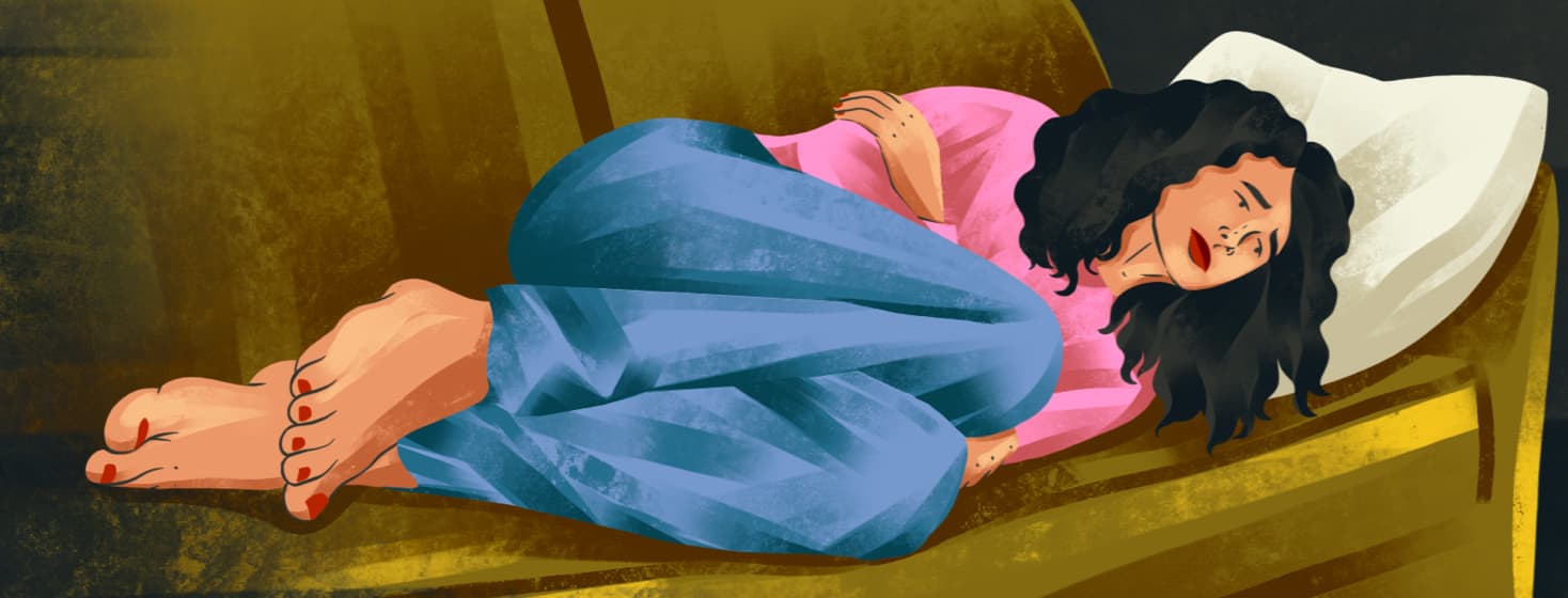 a nauseous woman curled up on a couch clutching her stomach